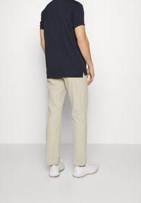 Miesten tummansininen lyhythihainen t-paita, yhdistettynä vaaleanbeigeihin housuihin ja valkoisiin urheilukenkiin. Yksinkertainen, rento malli, ei näkyviä kuvioita.