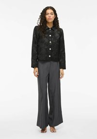 Veste noire brodée de fleurs avec un col et des boutons argentés, associée à un pantalon gris à jambes larges et des sandales argentées à enfiler.
