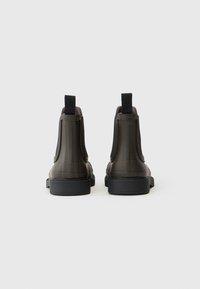 Bottines en simili cuir marron avec des panneaux élastiques sur les côtés, bout rond et semelle en caoutchouc noire. Dotées de languettes de tirage pour un enfilage facile.