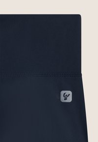 Leggings azul marino con una textura suave, una cinturilla ancha y un pequeño logo plateado en el lado inferior. Las costuras son visibles a lo largo de la cinturilla.