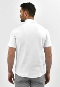 Witte polo met korte mouwen, een spreidkraag en een rechte onderkant. Glad textuur, minimale details en een klassieke pasvorm.
