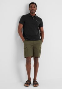 Black polo shirt, olive green cargo shorts, and black sandals. Shirt features a small logo; shorts have two side pockets.