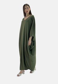 Abito kaftan oversize verde oliva con maniche corte, scollatura a V e design fluido, abbinato a sandali bianchi con tacco a blocco.