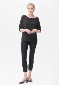 Schwarzes metallisches kurzärmeliges Oberteil und enganliegende schwarze Hose, getragen mit schwarzen High Heels. Glatte Textur und lockere Passform des ganzen Outfits.