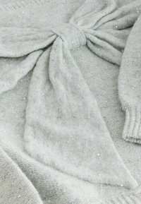Hellgrauer Pullover aus weichem Strickmaterial, mit einem gebundenen Schleifenelement an der Taille, das mit kleinen glitzernden Pailletten durchzogen ist.