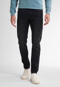 Czarne jeansy denimowe o dopasowanym kroju, z pięcioma kieszeniami i subtelnymi detalami w szwie, zestawione z białymi trampkami i jasnoniebieską bluzą.