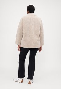 Beige fluffy faux fur jacket with a collar and long sleeves, shown from the back, paired with black pants and white sneakers.