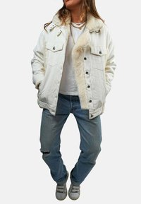 Veste en denim blanc avec un col en fausse fourrure, dotée de poches avant, de boutons en argent et d'une coupe décontractée, assortie à un jean bleu clair.