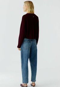 Bordeaux cropped trui met een textuurafwerking, gecombineerd met lichtblauwe high-waisted jeans met achterzakken en een relaxte pasvorm.