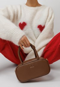 Person wearing a white fuzzy sweater with red hearts and red pants, holding a brown leather RYŁKO handbag by its handle.