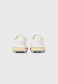 Zapatillas con parte superior de malla blanca, acentos en amarillo y gris, y suela de goma texturizada con studs salientes para tracción.