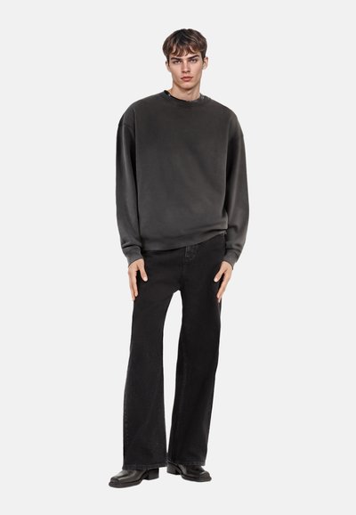 Donkergrijze sweatshirt met een ronde halslijn, losse pasvorm en geribbelde manchetten, gecombineerd met zwarte flared corduroy-broeken en chunky zwarte laarzen.