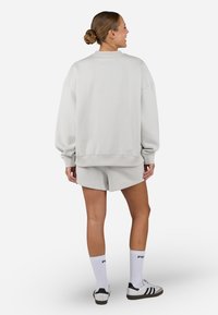 Light gray oversized sweatshirt paired with matching shorts. Features ribbed cuffs and hem, with white socks and black-accented sneakers.