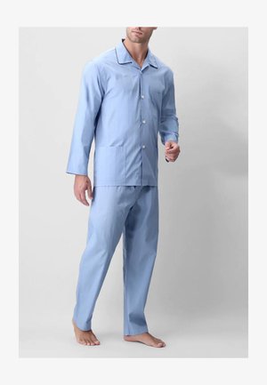 Uomo che indossa una camicia da pigiama azzurra a maniche lunghe con bottoni e colletto, abbinata a pantaloni larghi, in piedi a piedi nudi su sfondo neutro.