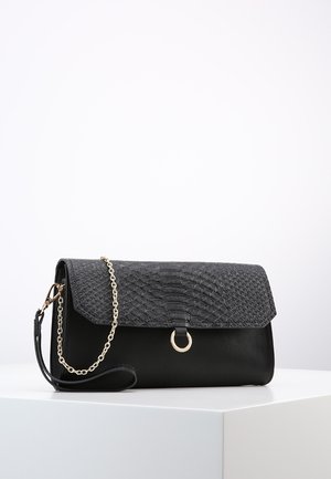 Sort clutch-taske med tekstureret flap, guld ringdetalje og aftagelig guld kæde rem, der hviler på hvid overflade mod lys baggrund.