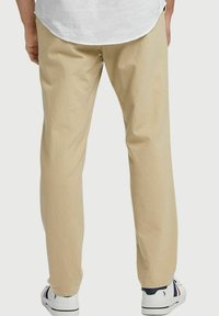 Beige katoenen broek met een slim fit, een manchet aan de onderkant en een subtiele textuur, gecombineerd met witte sneakers met blauwe en rode accenten.