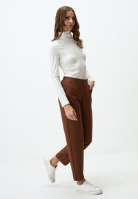 Maglione bianco a maniche lunghe con collo alto, pantaloni marroni a gamba tapered e sneakers bianche. Tessuto liscio, design aderente, vita media, tasche laterali.