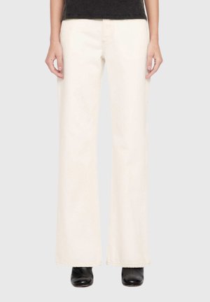 Lower body of a person wearing off-white wide-leg pants, black boots, and a black top against a plain light background.
