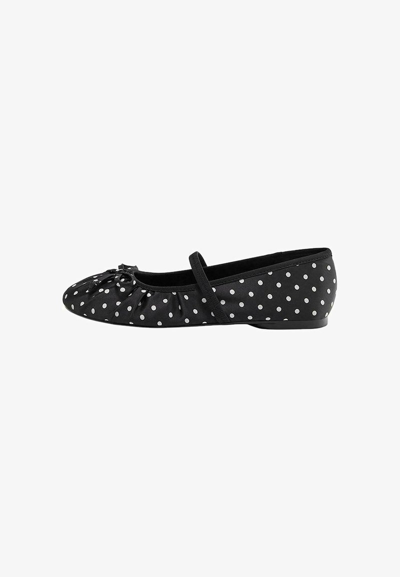 Chaussure de ballet plate noire avec des pois blancs, une fine sangle sur le pied et un petit nœud sur l'orteil arrondi.