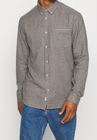 Bruine geruite overhemddas van katoen, met een enkele borstzak en een kraag. G gedragen met blauwe spijkerbroek.