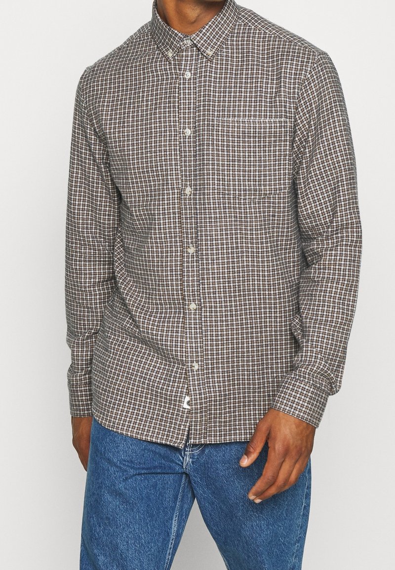 Bruine geruite overhemddas van katoen, met een enkele borstzak en een kraag. G gedragen met blauwe spijkerbroek.