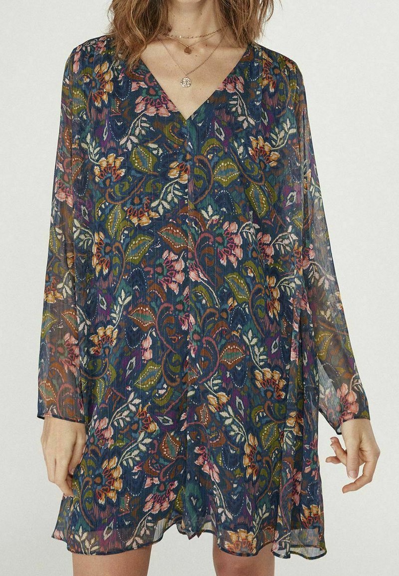 Robe transparente à motif floral, manches longues, col en V profond et silhouette décontractée dans des tons bleu foncé, vert, rose et orange.