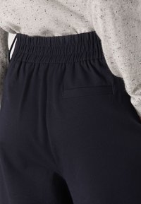 Sötétkék, elasztikus derékrésszel rendelkező nadrág sima textúrával, kis, téglalap alakú hátsó zsebbel. A szövet könnyűnek és légáteresztőnek tűnik.