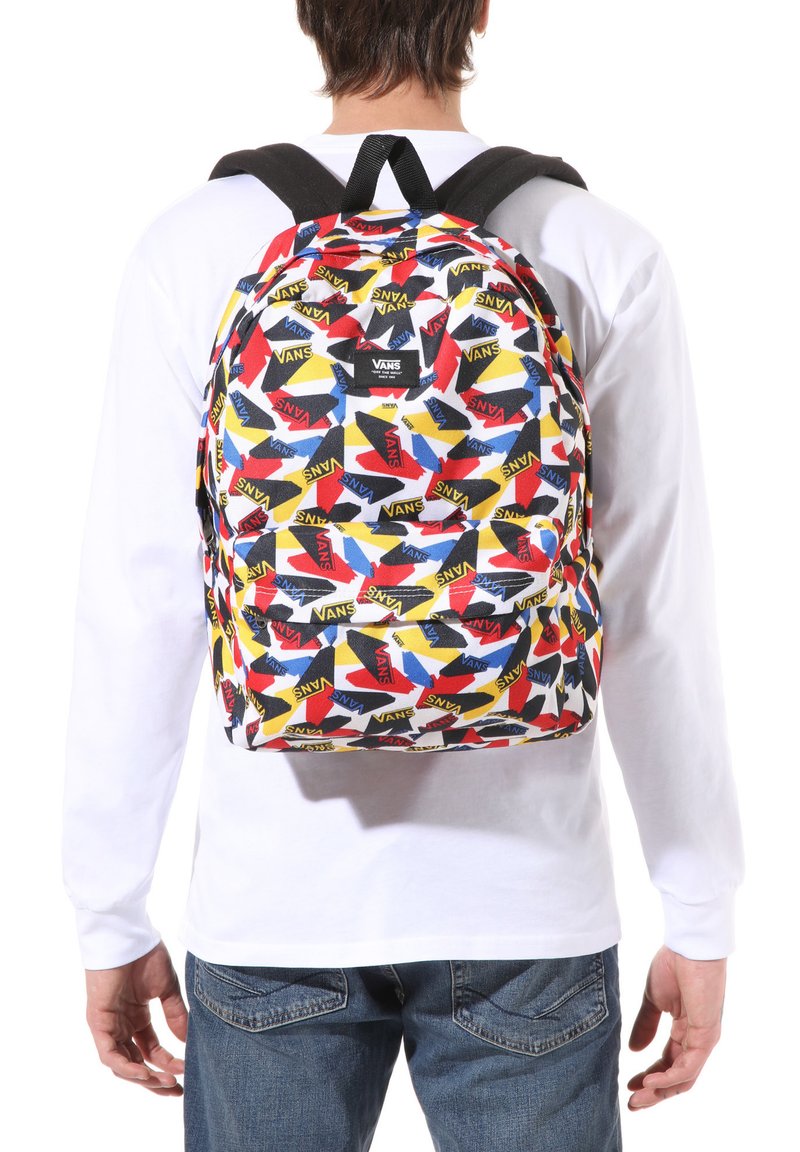 Mochila Vans multicolor con un patrón de logotipos repetidos en rojo, amarillo y azul sobre un fondo blanco, con correas ajustables negras.