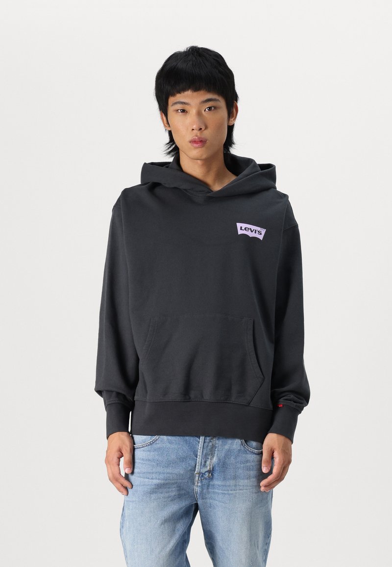 Sudadera negra con capucha y un bolsillo frontal, con un logo morado de Levi's en el pecho y puños acanalados. Se lleva con jeans de mezclilla azul claros.