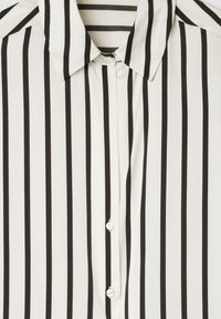 Blusa a righe bianche e nere con colletto, dotata di bottoni lucidi e un tessuto leggero e morbido. Le righe verticali predominano nel design.