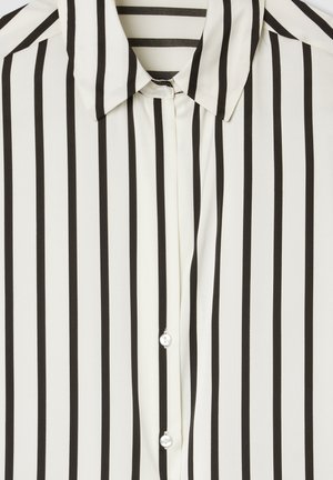 Blusa a righe bianche e nere con colletto, dotata di bottoni lucidi e un tessuto leggero e morbido. Le righe verticali predominano nel design.