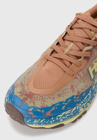 Leichte Laufschuhe mit einem gemusterten Mesh-Obermaterial in Grün und Braun, braunen Lederakzenten, blauer Außensohle und strukturiertem Zwischensohlenmaterial.