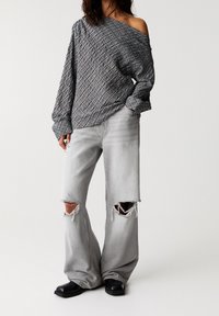 Haut gris à motifs, épaules dénudées, manches longues, associé à un jean gris clair déchiré à jambes larges et des bottines noires.