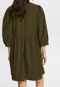 Vestito verde scuro, lungo fino al ginocchio, con maniche a sbuffo, vita arricciata e tessuto morbido. Design semplice senza motivi o decorazioni visibili.