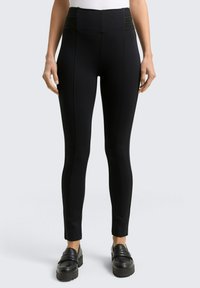 Zwarte high-waisted legging met geribbelde accenten op de taille, gemaakt van rekbare stof. Strak ontworpen met stiksels langs de zijkanten.