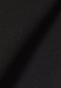 Close-up van zwarte textuurstof met een fijn, dicht geweven patroon en subtiele schaduwen die de plooien benadrukken.