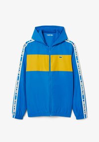 Blauwe zip-up hoodie met een gele horizontale streep over de borst, witte accenten op de mouwen en een klein groen krokodillenlogo.