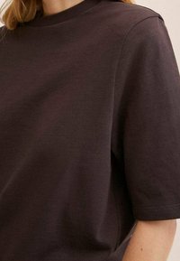 Mørkebrun bomulds t-shirt med rund halsudskæring, korte ærmer og en afslappet pasform. Glat tekstur uden synlige mønstre eller udsmykninger.