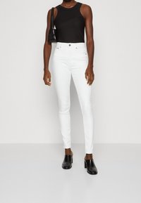 Jeans ajustados blancos de denim, con una cintura alta y corte regular. Combinados con una blusa sin mangas negra y mule de tacón negro.