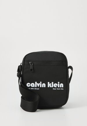 Black crossbody bag made of nylon with a zippered compartment; features white branding text and an adjustable strap.