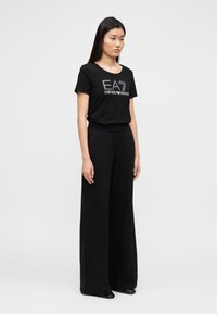 Μαύρο T-shirt με το λογότυπο "EA7 Emporio Armani" στο εμπρός μέρος, συνδυασμένο με μαύρο φαρδύ παντελόνι με ελεύθερη ροή. Λείο ύφασμα, απλός σχεδιασμός.
