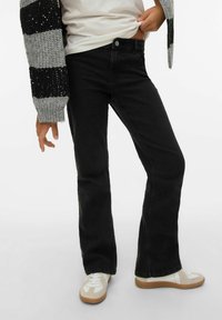 Svarta jeans med utsvängda ben i denim, med standarddesign med fem fickor och knappstängning, kombinerade med vita sneakers.