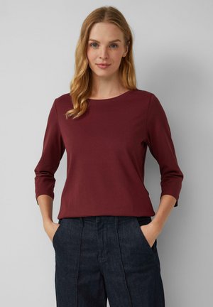 Chemise bordeaux à manches longues avec un col rond, en tissu doux. Associée à un pantalon en denim foncé avec des poches latérales.