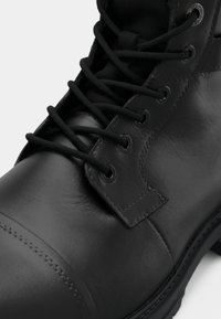 Bota de piel negra hasta el tobillo con cordones redondos, un acabado texturizado y costuras reforzadas, con una suela de goma resistente y ojales de metal.