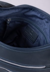 Navy leather bag interior featuring a zippered pocket and a textured logo patch. Smooth fabric lining with contrasting stitching details.