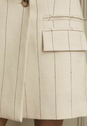 Blazer beige texturizado con rayas verticales negras, que presenta un cierre de botón y un gran bolsillo lateral con detalle de solapa.