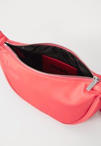 Marsupio in nylon di colore corallo con chiusura a zip. L'interno presenta uno scomparto per carte brandizzato. Texture liscia con dettagli in metallo argentato.