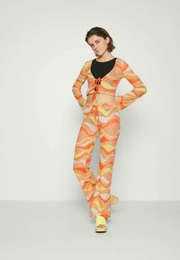Conjunto de duas peças com padrão ondulado em laranja e amarelo. A parte de cima apresenta um nó na frente e mangas longas, combinando com calças largas. 