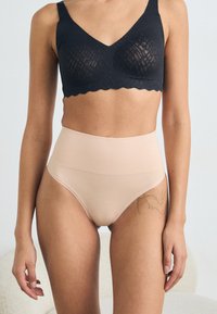 Black lace bralette with a scalloped edge, paired with high-waisted nude seamless underwear. Smooth texture and fitted design.