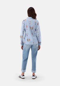 Light blue long-sleeve shirt with illustrated figures, paired with light blue cuffed jeans and white sneakers with black stripes.